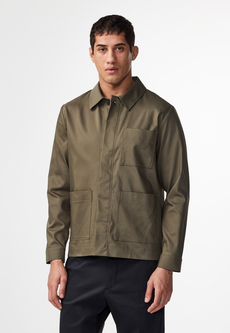 Zielono-oliwkowa kurtka wykonana z gładkiego materiału, z kołnierzykiem, zapięciem na guziki z przodu i dwiema dużymi kieszeniami z przodu.