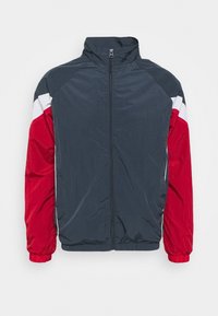 Tuulitakki tummansinisellä vartalolla, punaisilla hihoilla ja valkoisilla yksityiskohdilla. Varustettu korkealla kauluksella ja elastisilla hihoilla tiukan istuvuuden saavuttamiseksi.