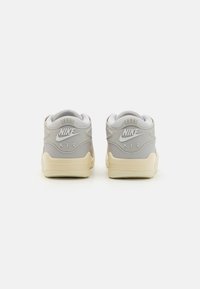 Baskets Nike Air, présentant un design gris clair et crème, une tige texturée, un col rembourré et un détail visible de l'amorti Air.