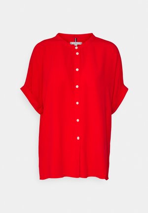 Camiseta de manga corta de color rojo brillante con cuello redondo, botones blancos en la parte delantera y puños remangados, mostrada sobre un fondo blanco liso.