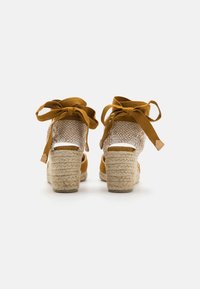 Hnědé espadrilky na klínu s juteovou patou, textilním svrškem a šněrováním kolem kotníku. Obsahují texturovanou otevřenou síťovou část vzadu.