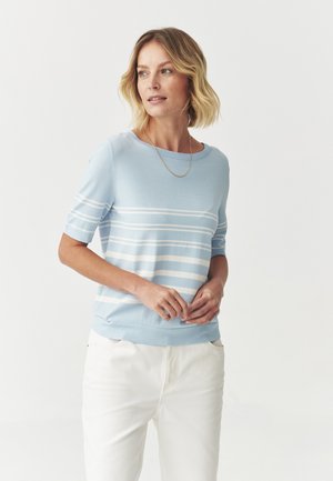 Pull over court bleu avec des rayures blanches horizontales. Doté d'un col rond et d'une texture en tricot doux. Assorti avec un pantalon blanc.
