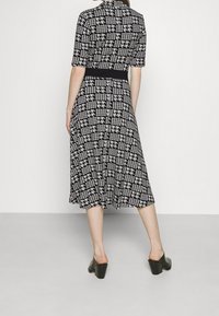 Robe midi à motifs en noir et blanc avec des manches courtes, taille cintrée et jupe évasée. Le matériau semble lisse avec un motif pied-de-coq.