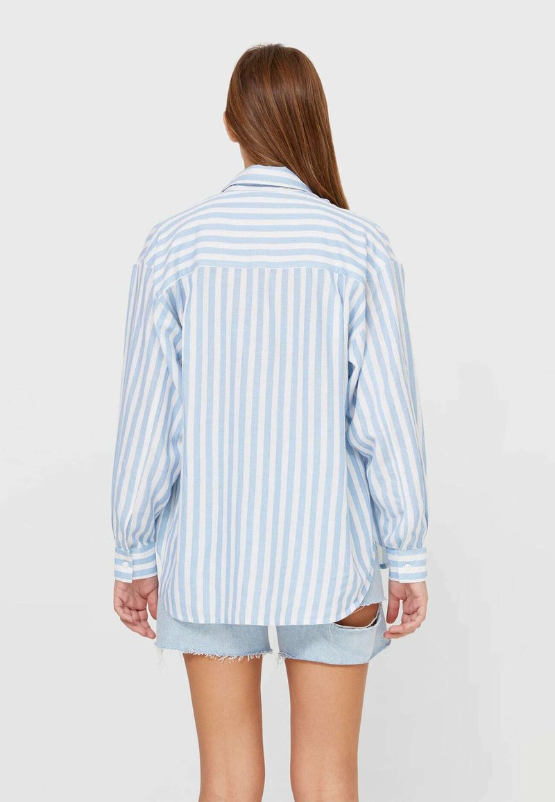 Niebiesko-biały koszula w paski z guzikami, z bawełnianego materiału, luźny krój, z długimi rękawami i zaokrąglonym dołem, w połączeniu z dżinsowymi szortami.