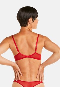 Soutien-gorge rouge en tulle avec bretelles réglables et fermeture au dos. Présente une texture lisse et un design minimaliste sans rembourrage.