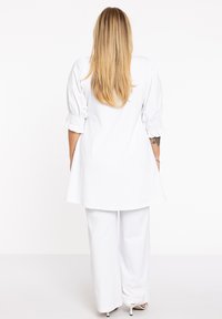 Weißes Oberteil mit Puffärmeln und gerafften Bündchen, kombiniert mit weit geschnittenen weißen Hosen. Glatte Textur, minimalistisches Design, geeignet für legere Anlässe.