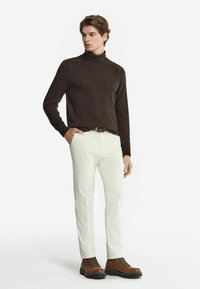 Brun stickad polotröja, vita texturerade byxor, bruna snörstövlar. Enkelt mönster, ribbade fållar och inga synliga mönster.