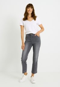 Vaqueros grises de talle alto con diseño de pierna recta, combinados con una camiseta blanca de cuello en V y zapatillas blancas, mostrando un estilo casual.