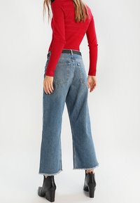 Blaue Denim-Jeans mit weitem Bein und ausgefransten Säumen, kombiniert mit einem roten, gerippten Langarmshirt und schwarzen, hochhackigen Stiefeletten. Glatte Textur, legerer Schnitt.