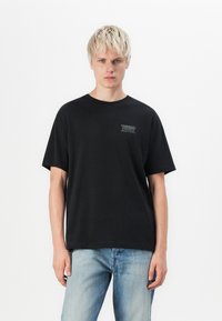Sort bomulds t-shirt med rund hals og korte ærmer; har et lille grønt og hvidt logo på venstre brystområde.