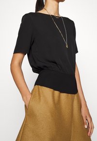 Blusa negra con mangas cortas y una cinturilla negra de canalé, combinada con una falda de color marrón dorado. Diseño minimalista, textura de tela suave.
