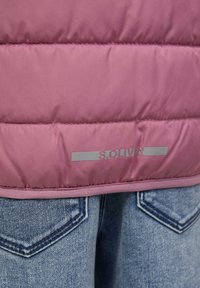 Rosa gesteppte Jacke mit reflektierendem "s.Oliver" Logo über den Gesäßtaschen von blauen Jeans.