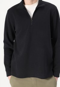 Pull-over noir à manches longues avec col à fermeture éclair quart. Fabriqué en matériau doux, doté d'une finition texturée et d'une coupe décontractée.