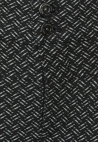 Svart stickat tyg med ett strukturerat zickzackmönster i ljusgrått. Två svarta knappar syns högst upp och tillför detalj till designen.