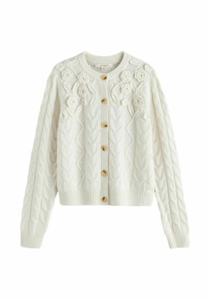 White knitted cardigan with wooden buttons, cable-knit pattern, and 3D floral decorations on the upper front and shoulders.