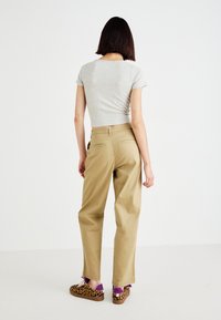 Pantaloni beige a vita alta con vestibilità rilassata, tasche posteriori; abbinati a una camicia grigia a maniche corte e scarpe slip-on con stampa animale.