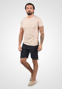 Bež majica s kratkim rukavima sa suptilnim uzorkom, u kombinaciji s tamnoplavim hlačama i svijetlim slip-on cipelama.