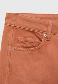 Denim tkanina boje hrđe s teksturiranim završetkom, s malim prednjim džepom, metalnim zakovicama i prošivenim detaljima na struku.