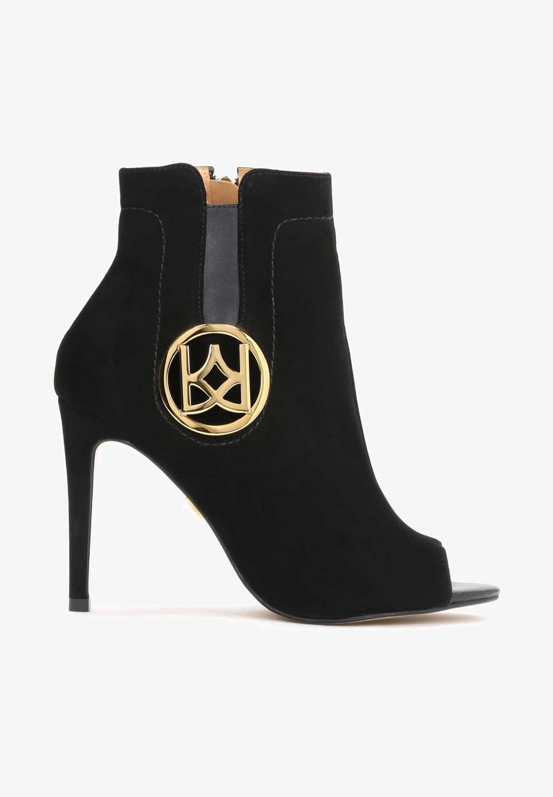 Bottines en cuir suédé noir à bout ouvert avec un talon haut, dotées d'un accent logo circulaire doré et d'une fermeture éclair à l'arrière.
