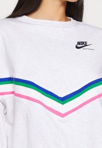 Valkoinen collegepaita, jossa on viistekuvio pinkeillä, vihreillä ja sinisillä raidoilla. Nike-logo mustana ylhäällä vasemmalla. Pehmeä pinta.