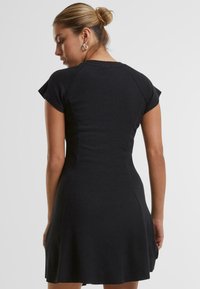 Robe noire à manches courtes avec une jupe évasée, fabriquée en matériau côtelé. Présente un corsage ajusté et une texture lisse, vue de l'arrière.