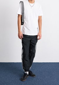 Bílé bavlněné tričko doplněné o černé nylonové běžecké kalhoty se třemi bílými pruhy po stranách a černé tenisky s texturovanými podrážkami.