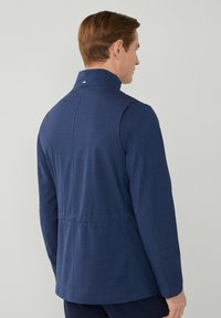Chaqueta tejida de color azul marino con cuello alto, corte estructurado y detalles en la costura trasera. Textura suave sin hardware visible ni patrones.