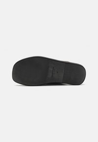 Black rubber shoe sole with a textured surface and smooth edges. Features a rectangular logo imprint near the center.