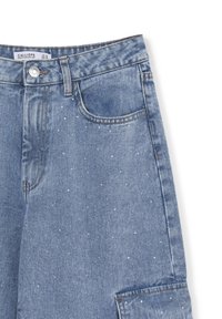 Jeans in denim azzurro chiaro con piccole borchie di metallo argentato sparse sul tessuto, dotati di tasca frontale e chiusura con bottone.