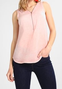 Haut sans manches rose clair avec un col en V et un zip central, fabriqué en tissu doux, avec un ourlet courbé et une coupe décontractée.