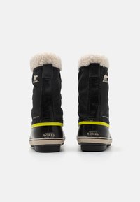 Botas impermeables negras con un cuello de forro polar, con acentos amarillos y una suela de goma. En la parte posterior se muestra el logo de Sorel.