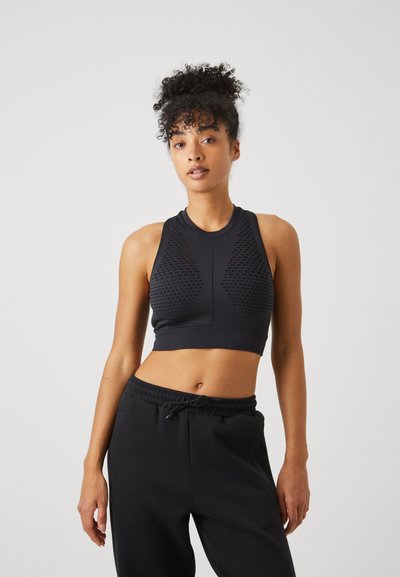 Fekete sportos crop top, textúrált hálós betétekkel, sima anyagú kivitelben és magas nyakkivágással, fekete zsinóros nadrággal párosítva.