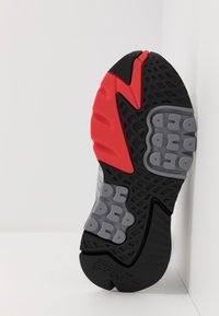 Černá a červená sportovní podešev s texturovanými vzory, gumovými úchyty a tlumícími prvky v šedé barvě, navržená pro trakci a pohodlí.