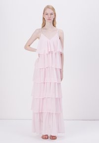 Világos rózsaszín maxi ruha, réteges, fodros alsó résszel. Áttetsző anyagból készült, vékony pántokkal és lebegő sziluettal rendelkezik.