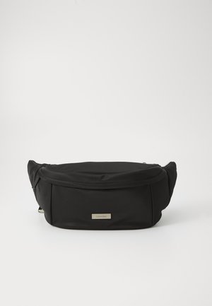 Zwarte nylon heuptas met een gladde textuur, gebogen vorm en een voorvak met rits. Beschikt over een gouden logo plaat.