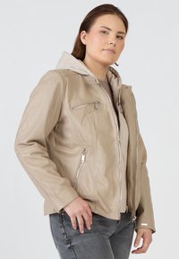Beige läderjacka med dragkedjefickor, avtagbar grå huva och en figurnära design. Slät textur med metalliska detaljer och sömnadsdetaljer.