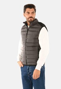 Gilet imbottito grigio con zip frontale, collo a camicia e spalle nere. Caratterizzato da cuciture orizzontali e due tasche laterali.