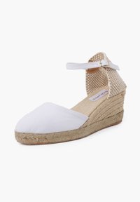 White canvas wedge espadrille with a jute heel, ankle strap, and a textured, woven upper for added detail.