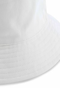 Fehér színű vászon fazonú kalap, jól látható varrásvonalakkal a karimán és texturált pamut anyagból.