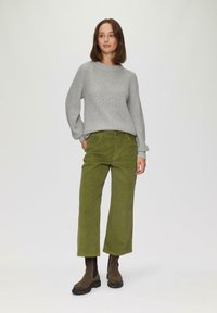 Grauer Strickpullover mit Rundhalsausschnitt, kombiniert mit olivgrünen Cordhose im weiten Bein und braunen Stiefeletten mit einer robusten Sohle.