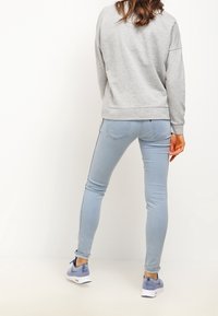 Sudadera gris, jeans ajustados azul claro y zapatillas azules. La sudadera tiene un corte relajado, mientras que los jeans presentan una textura suave y un ligero brillo.