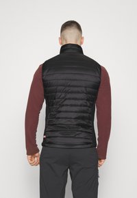 Sort oppustet vest med høj krave og vandret syninger, parret med en langærmet bordeaux top. Sidepaneler ikke synlige.