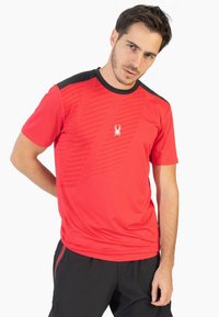 Camiseta deportiva roja con cuello negro, que presenta un patrón diagonal texturizado y un pequeño logotipo blanco en el pecho. Manga corta.