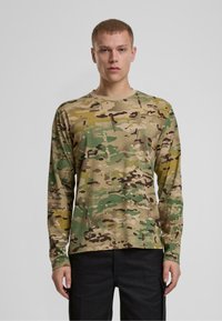 Majica dugih rukava u camo uzorku s nijansama zelene, smeđe i žute boje. Izrađena od teksturiranog materijala s dizajnom okruglog izreza.