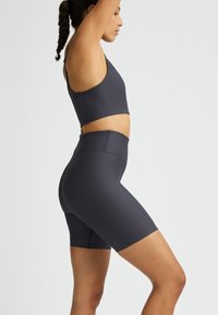 Mörkgrå sport-bh och högmidjade shorts, ribbad textur, åtsittande design, inga synliga logotyper eller mönster, bärs i en sidoprofilställning.