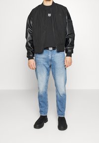 Černá bomber bunda s koženými rukávy, spárovaná s černým tričkem a modrými denimovými džíny. Černé kotníkové boty dotvářejí outfit.