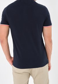 Polo shirt blu marina realizzato in cotone, con maniche corte e dettagli a righe rosse e bianche. Vestibilità classica con una texture liscia.