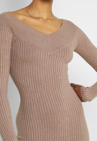 Abito in maglia a coste marrone con scollatura a V e maniche lunghe. Presenta una silhouette aderente e un tessuto testurizzato. Leggera lucentezza visibile.
