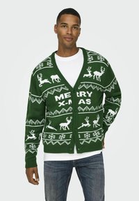 Grüner gestrickter Cardigan mit einem gemusterten Design von Rentieren und Schneeflocken, V-Ausschnitt und Knopfverschluss. Weißer "FROHE WEIHNACHTEN"-Text.
