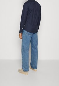 Camicia a maniche lunghe blu navy con dettaglio alla schiena, abbinata a jeans a gamba larga azzurri e calzature beige, con suola texture.